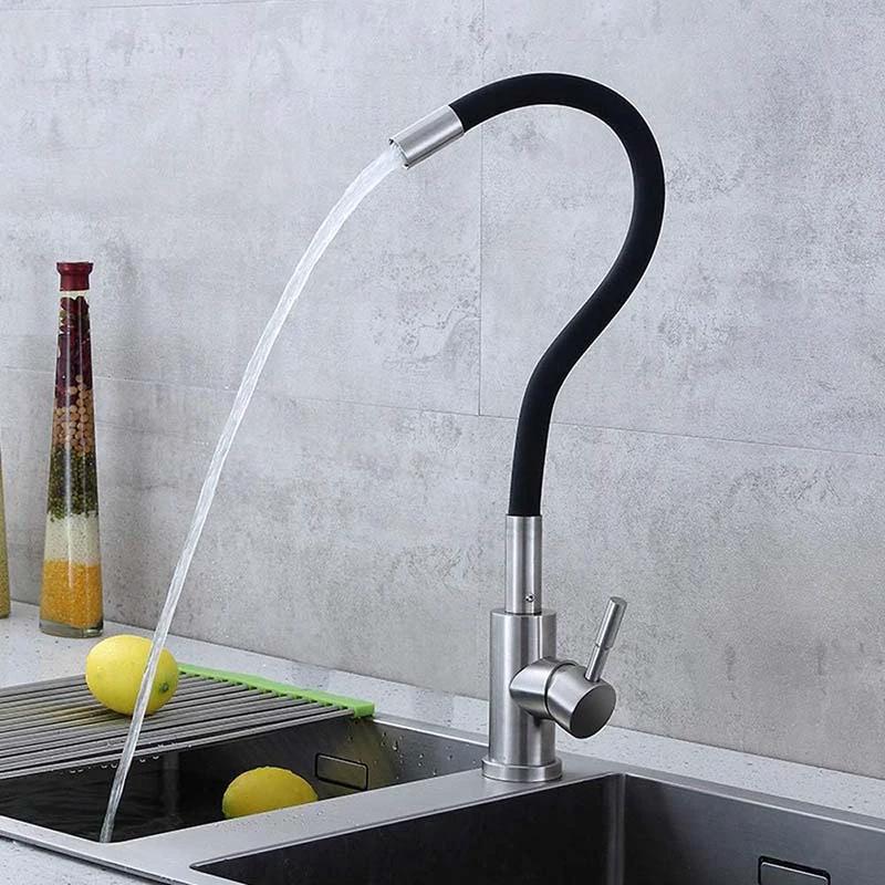 Modern kitchen faucet with water flowing into a sink against a gray tiled wall.