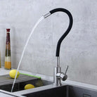 Modern kitchen faucet with water flowing into a sink against a gray tiled wall.