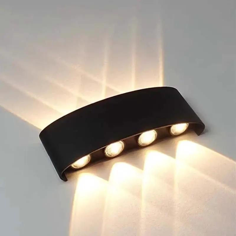 A curved black wall-mounted light fixture with four illuminated bulbs, casting warm light beams onto a light-colored wall.