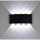 A modern black wall-mounted light fixture with three upward-facing and three downward-facing illuminated beams, shown against a textured white wall.
