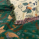 100% Cotton Reversible Throw Blanket draped over green and cream bird-pattern throws with fringe; decorative for sofa or bed.