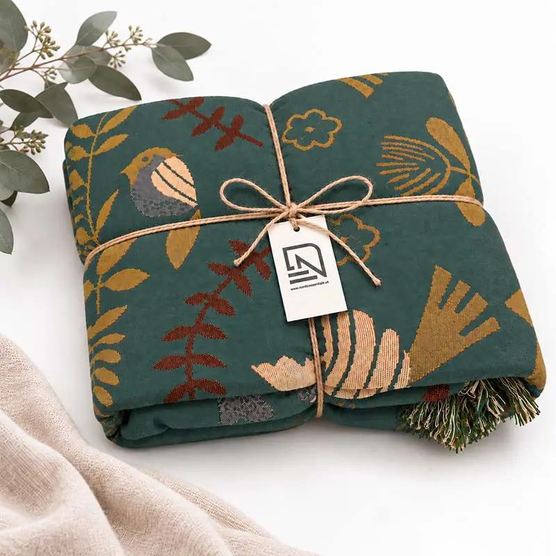 100% Cotton Reversible Throw Blanket, teal with birds and foliage, Nordic Essentials tag visible on folded throw