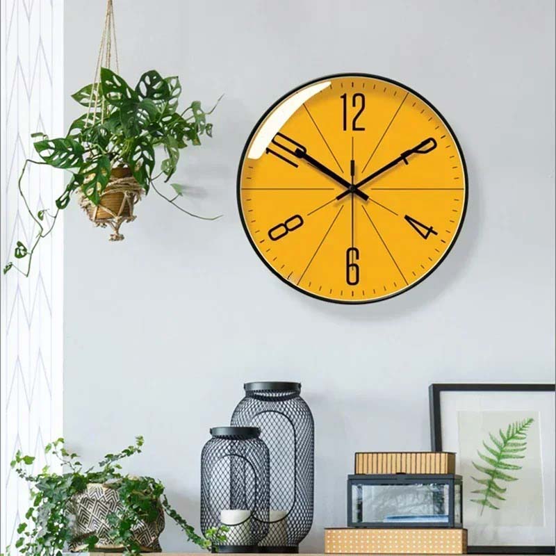 Wall Clock - yellow dial with black rim, hangs on a grey wall in a living room scene with plants.