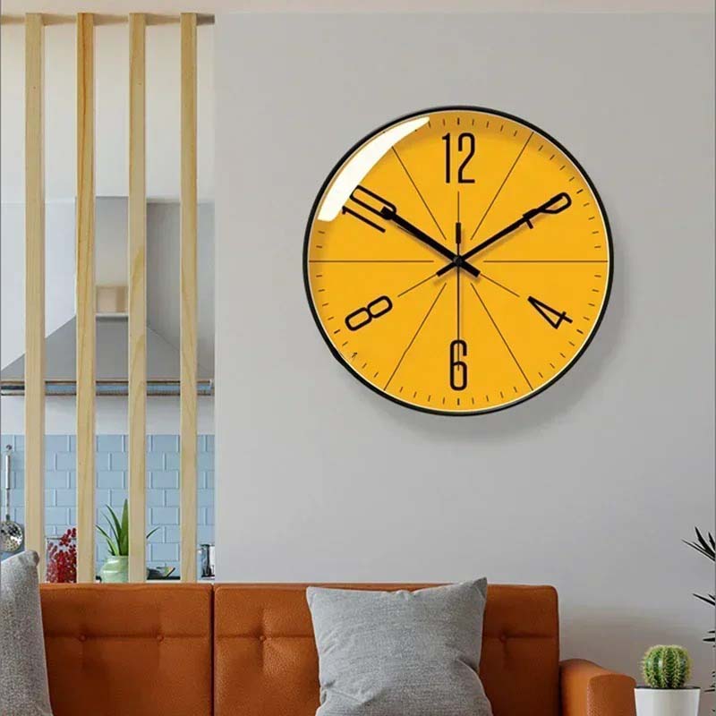 Wall Clock with yellow face and black frame mounted on a grey living room wall above an orange sofa.
