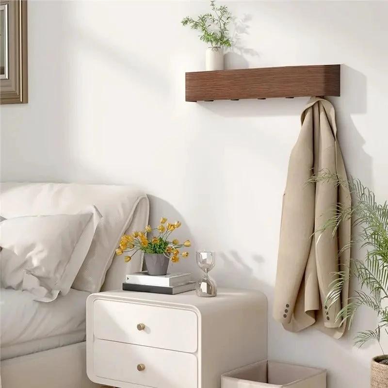 Wood & Iron Coat Rack with Hidden Hooks & Shelf mounted on a bedroom wall; coat hangs beside a nightstand.