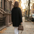 A model showcases a womens polished minimalist winter coat in a sleek black hue, styled with a high waisted outfit against a neutral background.