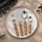 24-Piece Bamboo Handle Cutlery Set on a speckled ceramic plate; four bamboo-handled stainless steel utensils.