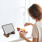Person eating from a bowl with a tablet stand displaying a blank screen on a white surface.