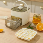 Ice cube tray with lid, ice cubes, and a glass of iced tea on a wooden surface.