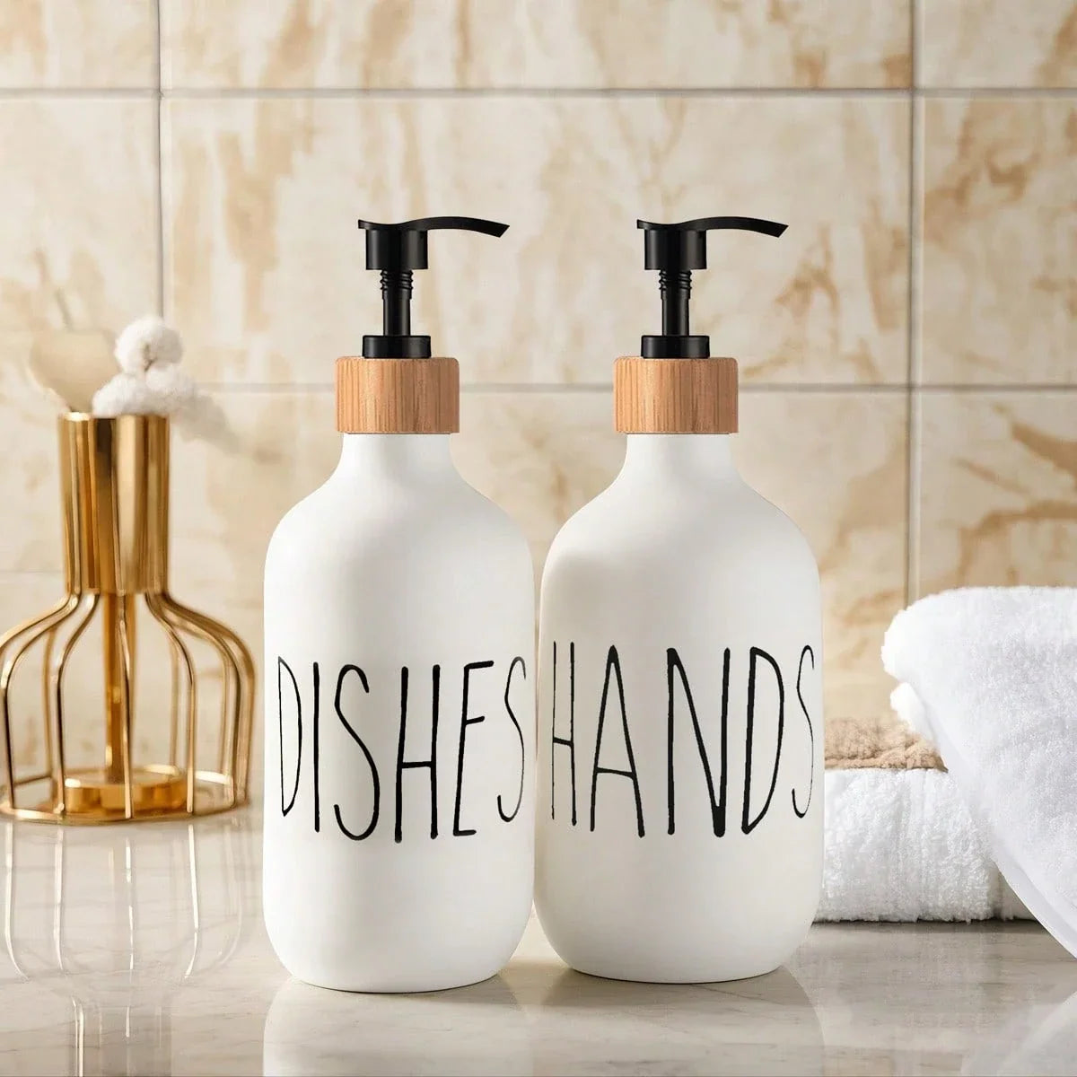 Two white soap dispensers with wooden caps labeled 'Dishes' and 'Hands' on a bathroom counter.